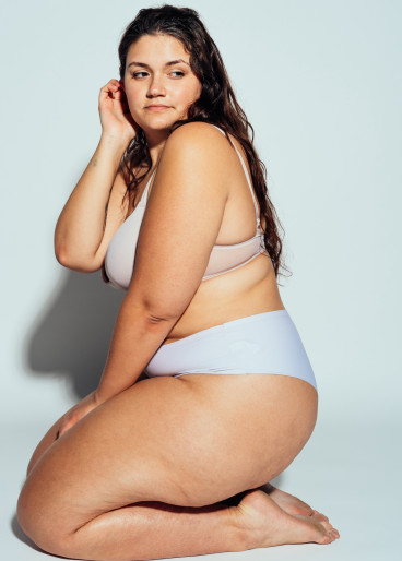 Eine stämmig, kräftige, dunkelhaarige Frau sitzend in Unterwäsche, auf Ihren Fersen.