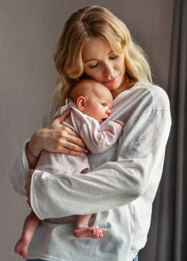 Eine blonde, junge Frau drückt Ihr Baby, liebevoll an Ihre Brust.